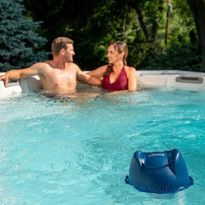 A couple relaxes in a pool with the FROG @ease Swim Spa Sanitizing System, surrounded by greenery, enjoying the benefits of mineral water and its self-regulating sanitizing experience utilizing SmartChlor Technology.
