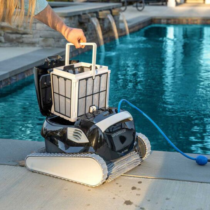 A person removes the filter basket from a Maytronics Dolphin Explorer E30 with WiFi Robotic Pool Cleaner 99996241-XPI beside a pool.