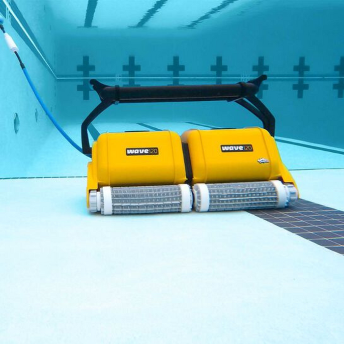A yellow Maytronics Dolphin Wave 120 Commercial Robotic Pool Cleaner (model 9999359-W120) is diligently cleaning the bottom of an empty swimming pool, showcasing its efficiency in pool maintenance.