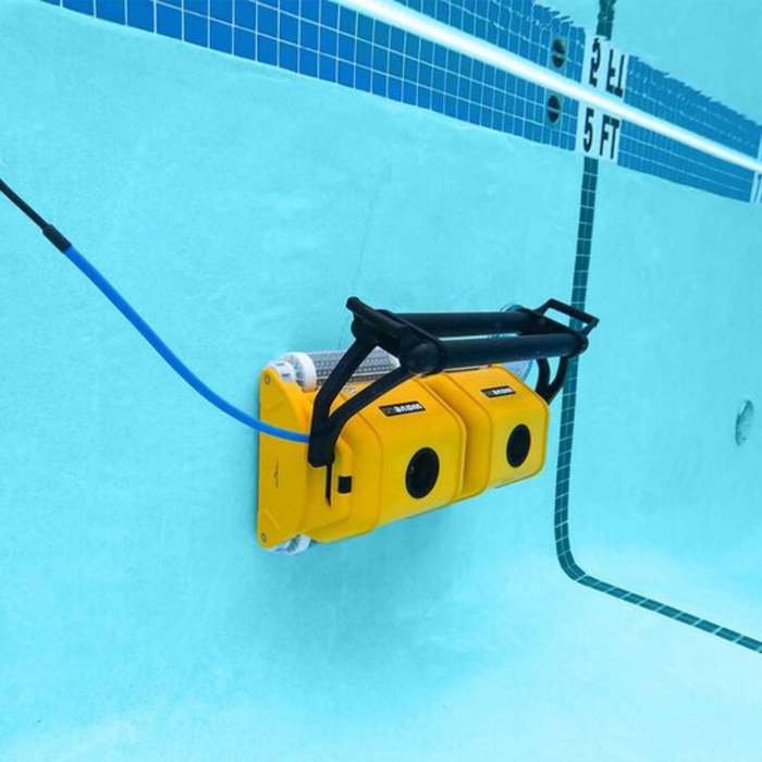 A yellow Maytronics Dolphin Wave 120 Commercial Robotic Pool Cleaner 9999359-W120 is attached to the side of an in-ground swimming pool with tile markers, ensuring effortless pool maintenance.