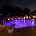 A nighttime pool scene featuring Pentair Pool's MicroBrite MULTI COLOR Pool Spa LED Lights, surrounded by water fountains and nearby lounge chairs.