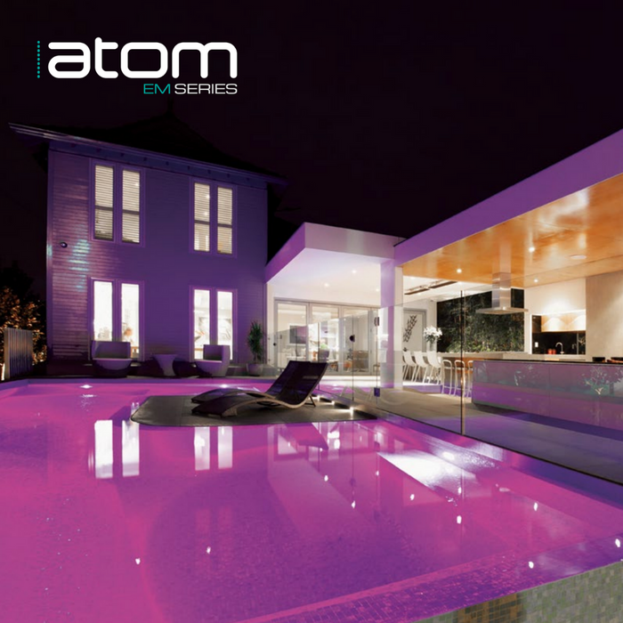 A modern house with a glowing pink-lit pool at night, enhanced by Spa Electrics ATOM EM Niche Style 3" LED Pool Lights' high-intensity Ceramic Light Engine. Text at the top left reads "atom EM SERIES".