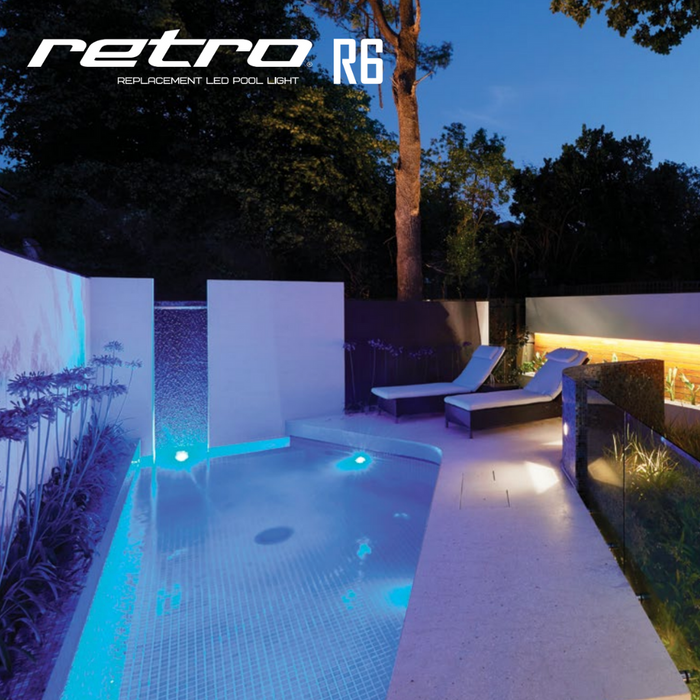 Immerse yourself in the contemporary ambiance of an outdoor pool illuminated by Spa Electrics' RETRO R6 Universal 6" Retro-Fit Pool Light. As dusk falls, these LED lights envelop the space in a tranquil glow. Find peace on two lounge chairs nestled among the trees, appreciating the UL Certified lighting system that blends safety with elegance.