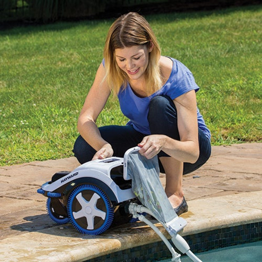 A woman in a blue shirt cleans a Hayward W3TVP700C TriVac 700 Top Skimming & Bottom/Wall Pressure Cleaner near the edge of a swimming pool on a sunny day.
